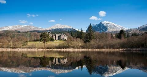 A castle beside a calm lake, with snowy mountains in the background.