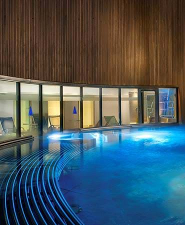 Modern spa hydro pool with curved design and waterfall feature, glowing in blue light.