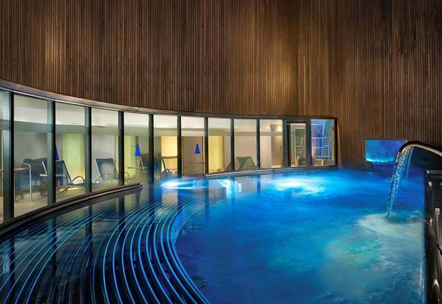 Modern spa hydro pool with curved design and waterfall feature, glowing in blue light.