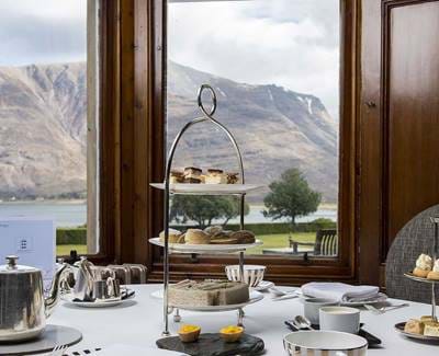 Afternoon tea set at The Torridon by a large window with a mountain and loch view in the background.