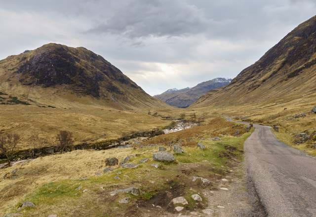 A rocky path through a valley with mountains in Perthshire looming in the distance, under dramatic skies.