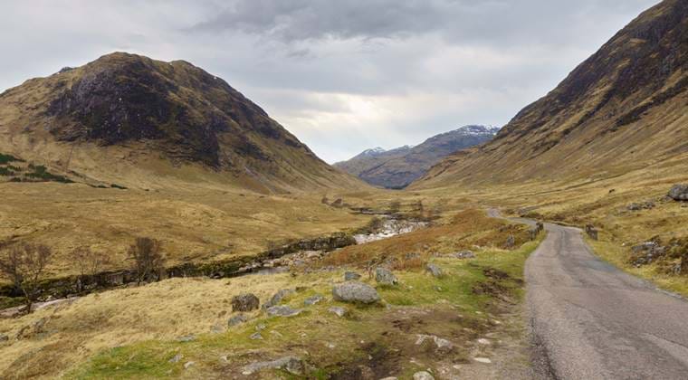 A rocky path through a valley with mountains in Perthshire looming in the distance, under dramatic skies.